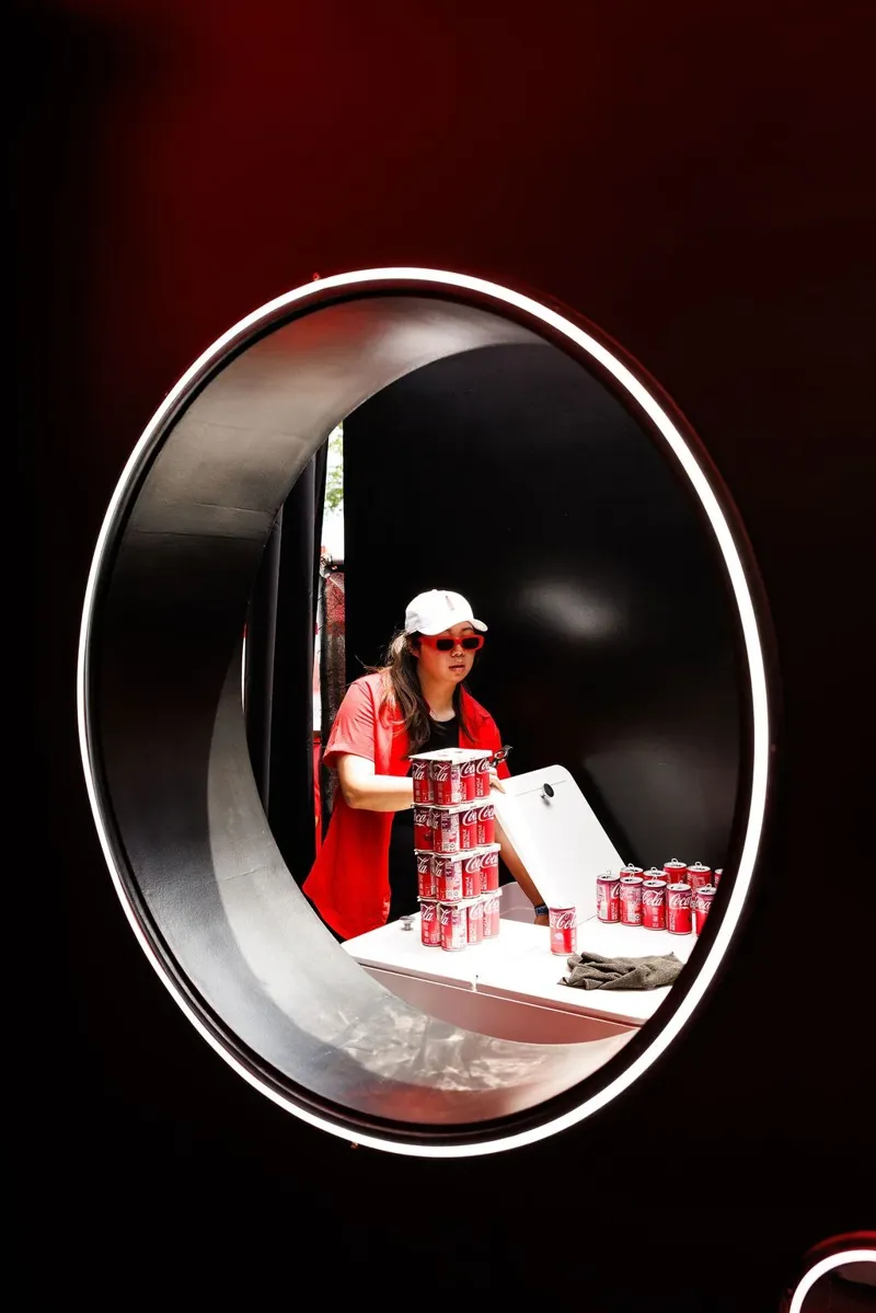 Staff stacking Coca-Cola cans through a lit porthole