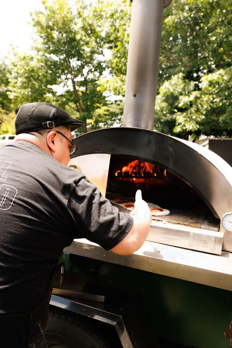 A chef sliding pizza into a wood-fired oven